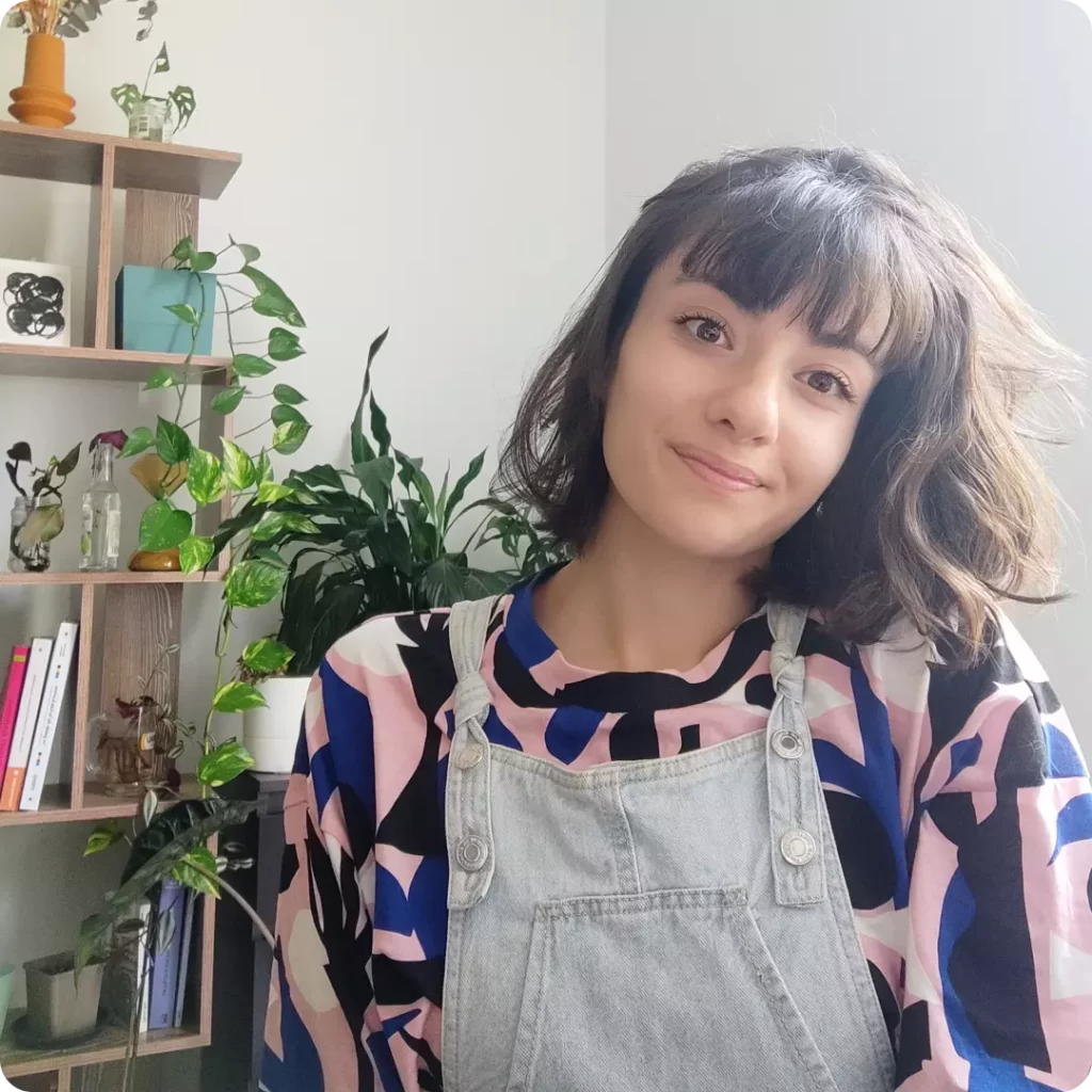 Photo de profil de Bérénice Bonnard avec en fond une étagère en bois, des livres et des plantes